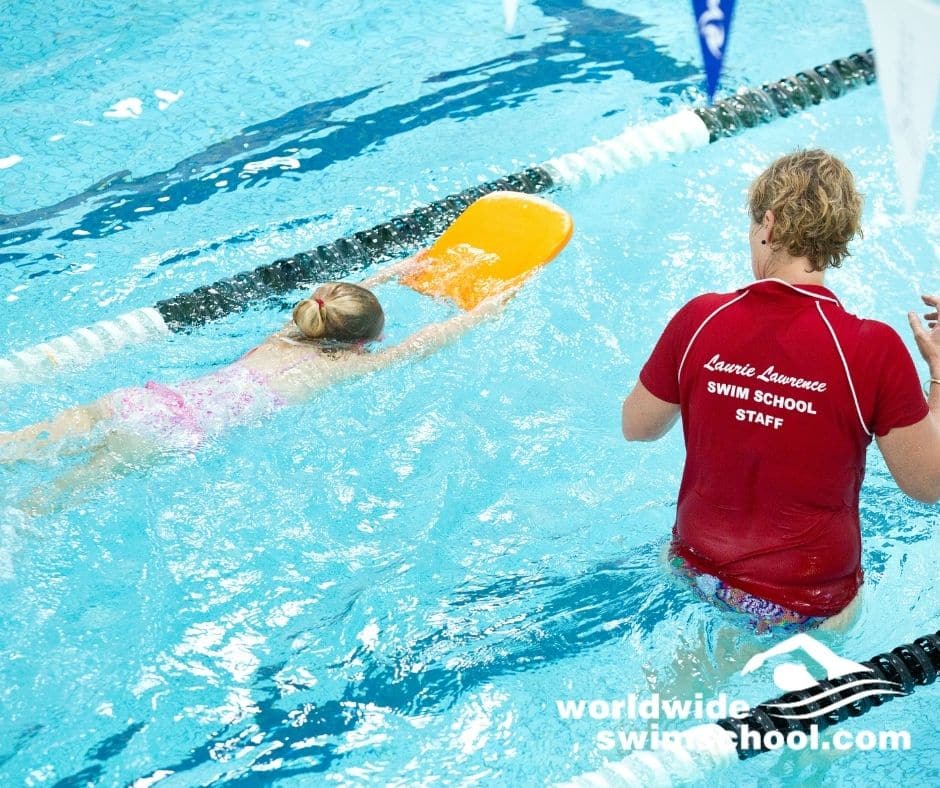 swim teaching in lane with learning holding kick board with face in water kicking