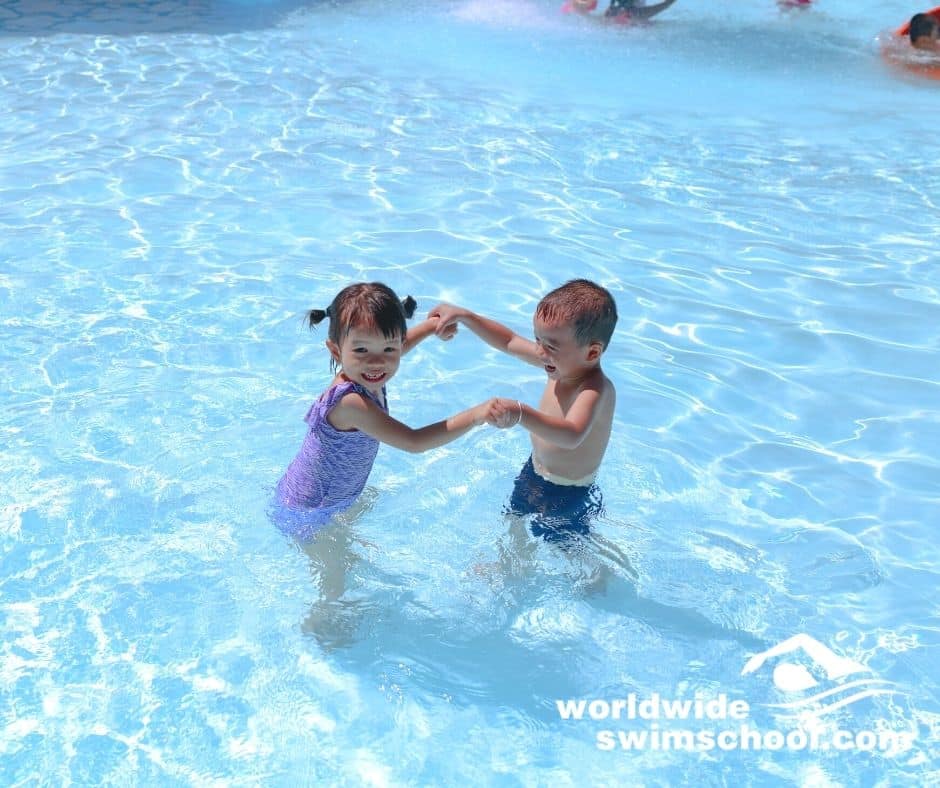 boy and girl holding hands playing in water swimming pool laughing happy