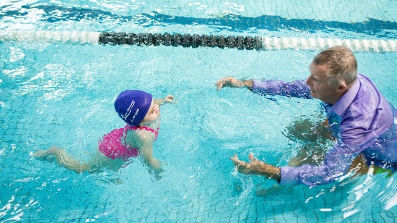 toddler swimming independently to teacher