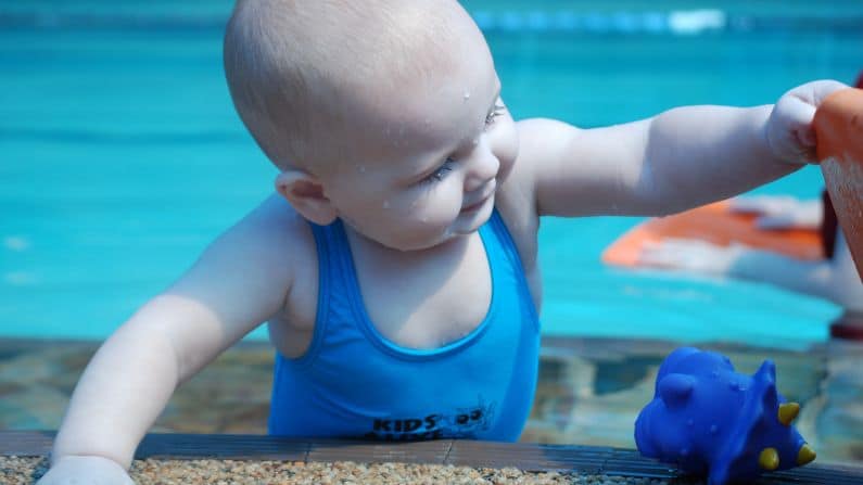 infant at side of pool putting toy in bucket 