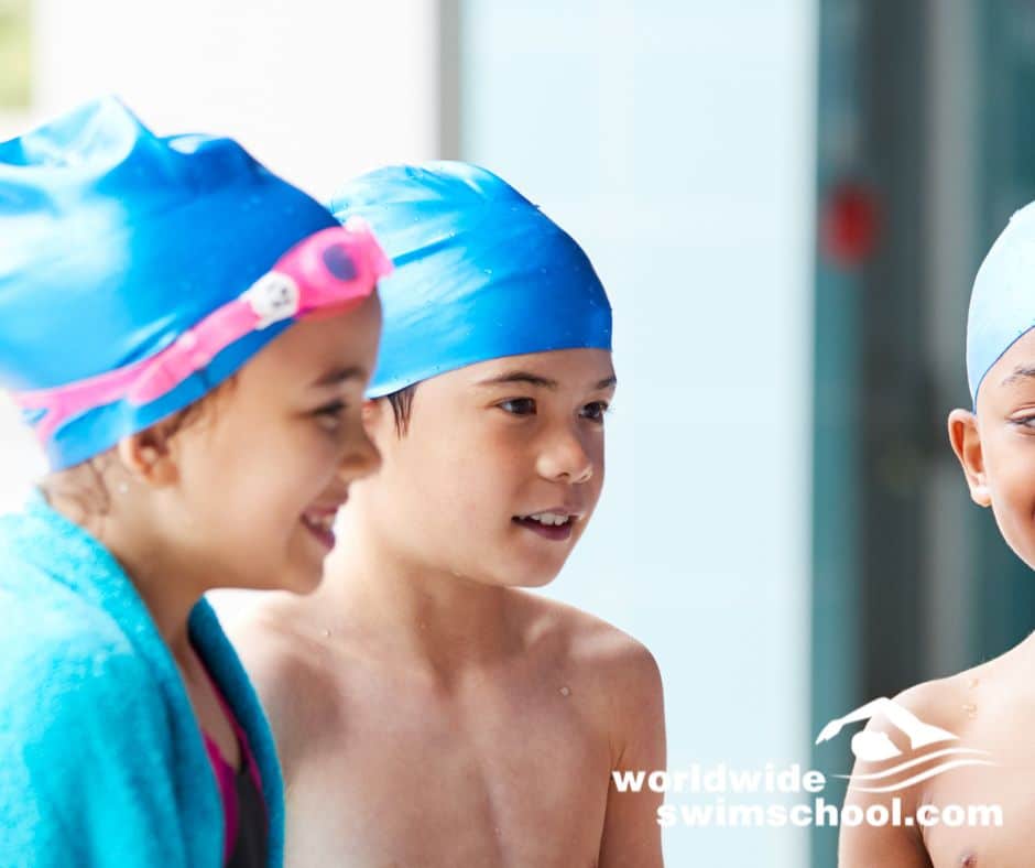 children wearing goggles and swim caps talking at pool