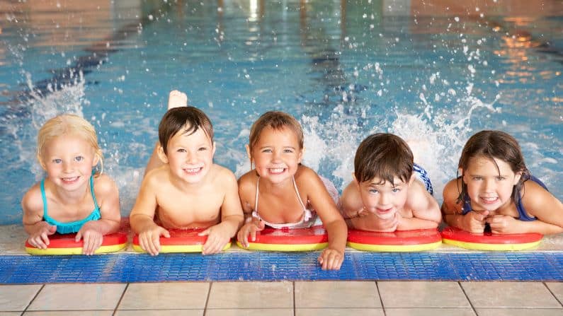 children smiling holding edge of pool kicking legs