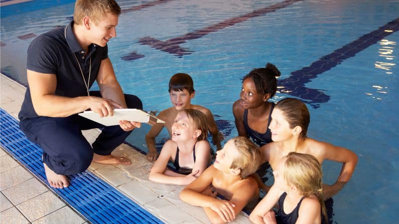 swim coach with lesson plan clipboard speaking swimmers in water