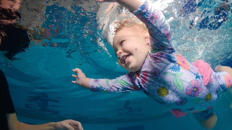baby daughter underwater in swimming pool happy smiling