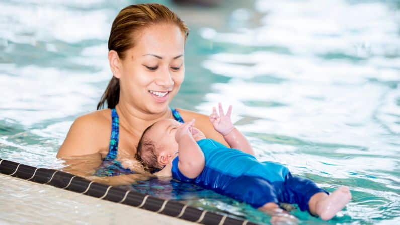 baby laying in swimming pool water with mother