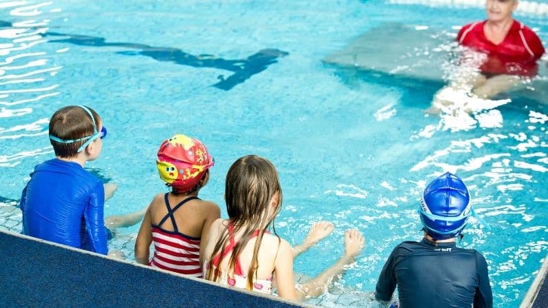 children looking at swimming teacher in pool water