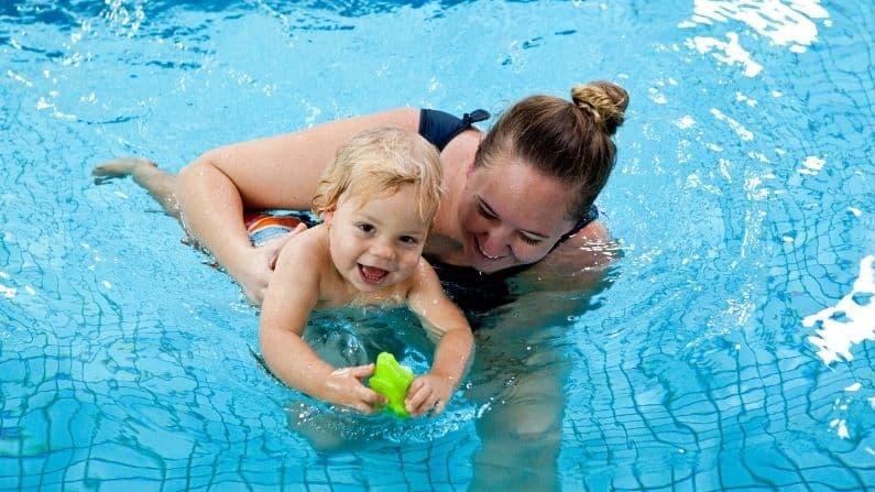 baby happy in water pool with toy with mother