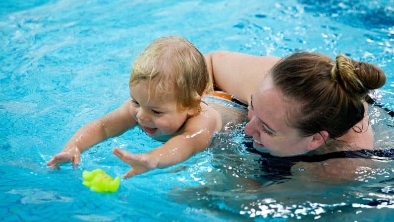mother with baby son in swimming pool chasing toy